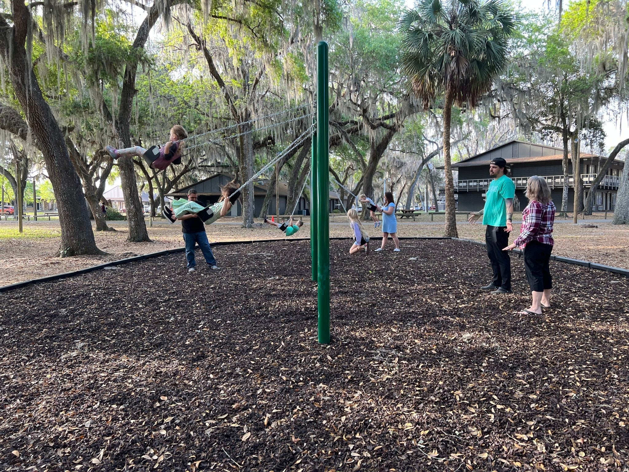 Children joyfully swinging on tall playground pole swing.