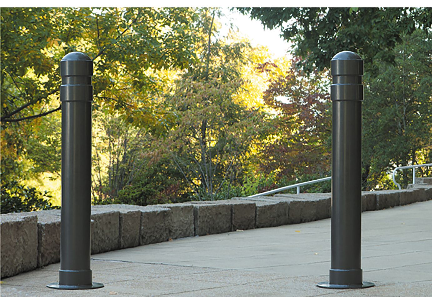 Lexington Series Bollard dark steel bollards with rounded tops along a paved walkway near stone edging and trees