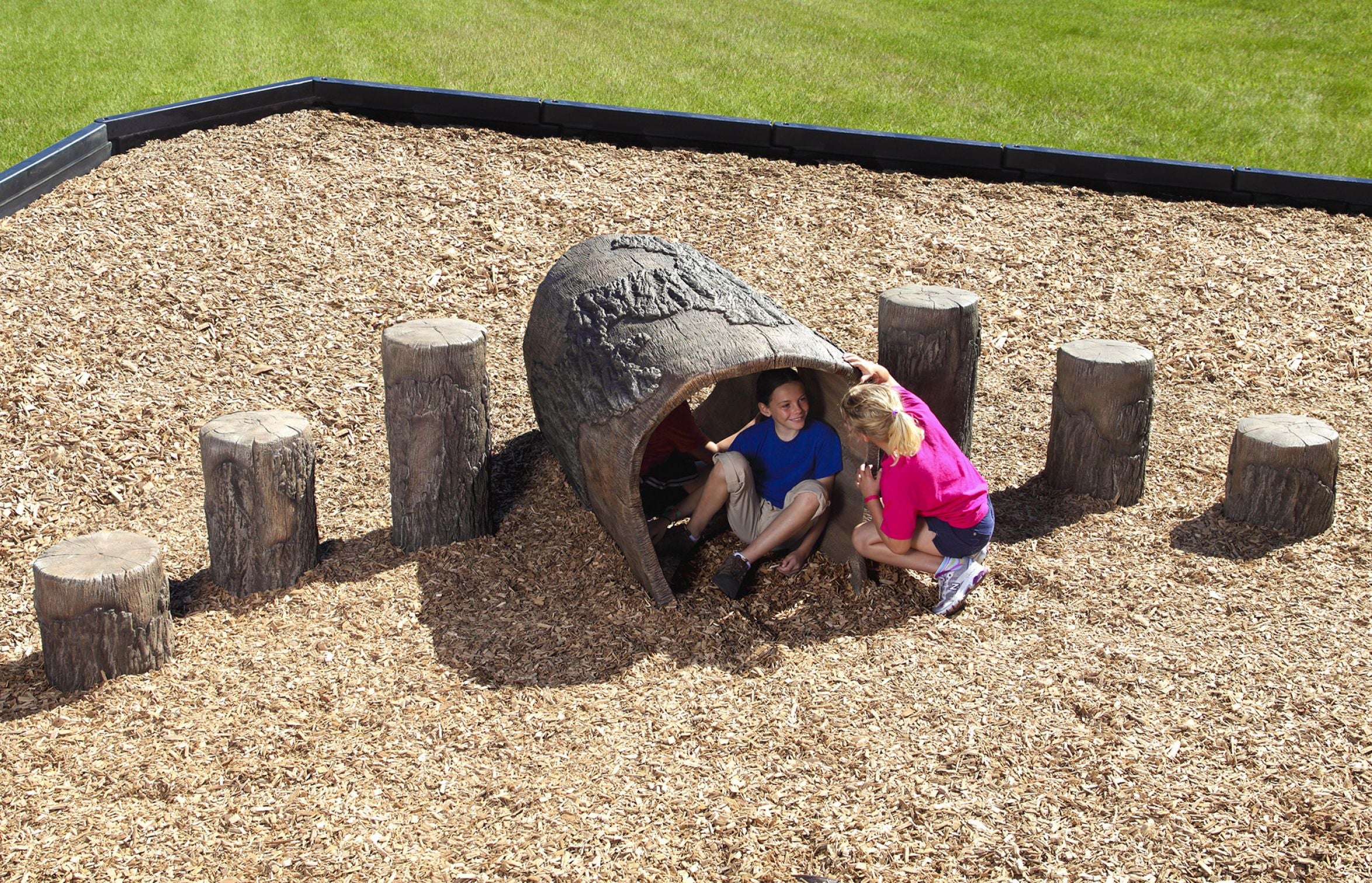 Nature Themed Playground Log Crawl Tunnel with children playing inside and around wood-textured climbing tunnel and tree stump seats on mulch