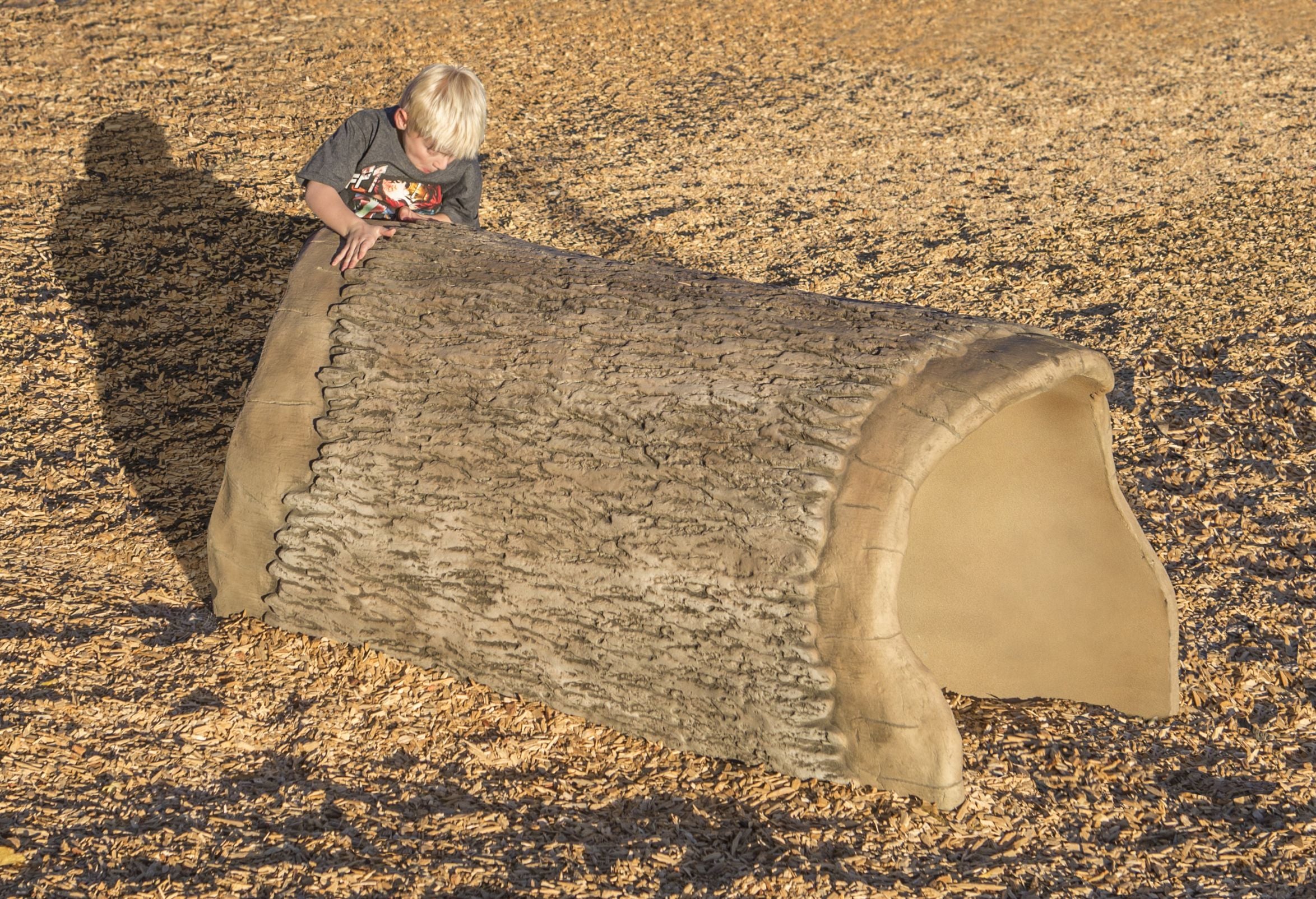 Child playing on a realistic wood grain playground log crawl tunnel on wood chip ground