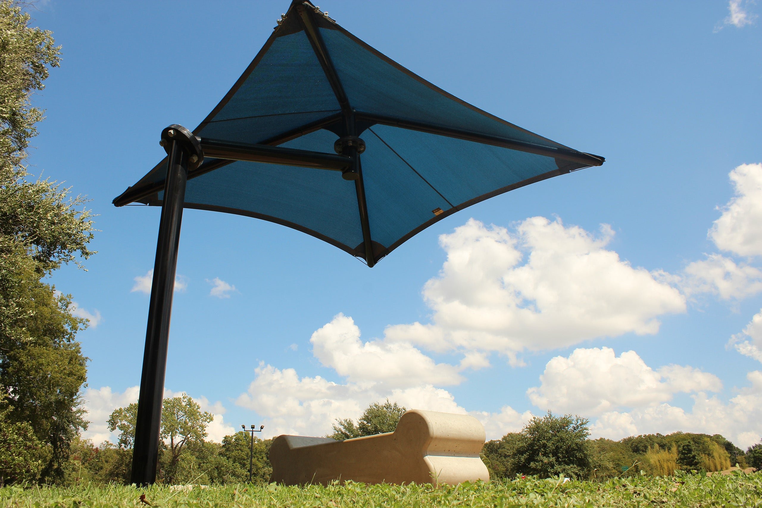 Single post cantilever shade structure with blue pyramid fabric canopy over outdoor bench in park setting