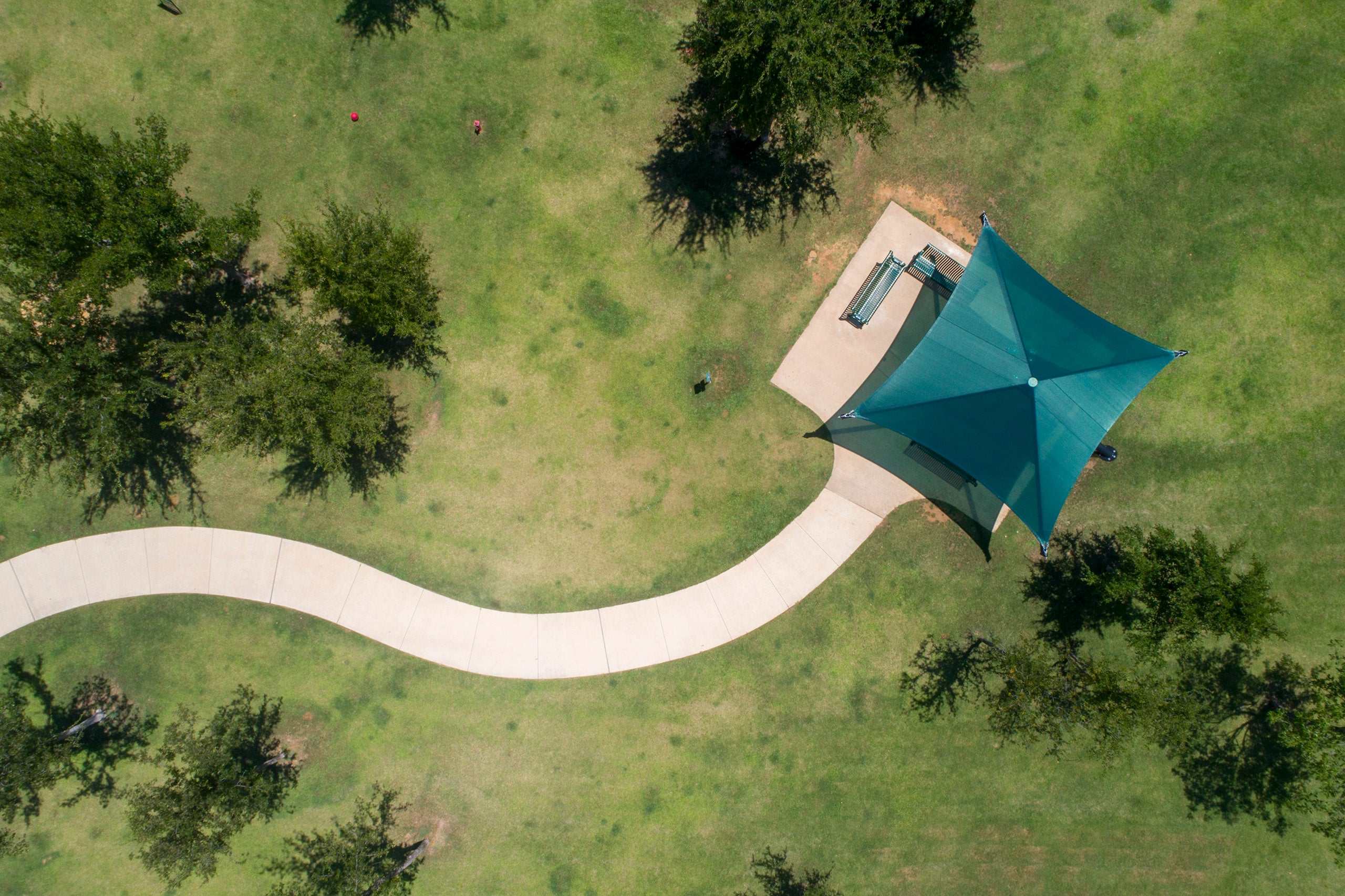 Overhead view of single post pyramid cantilever shade with green fabric covering concrete area with benches in grassy park