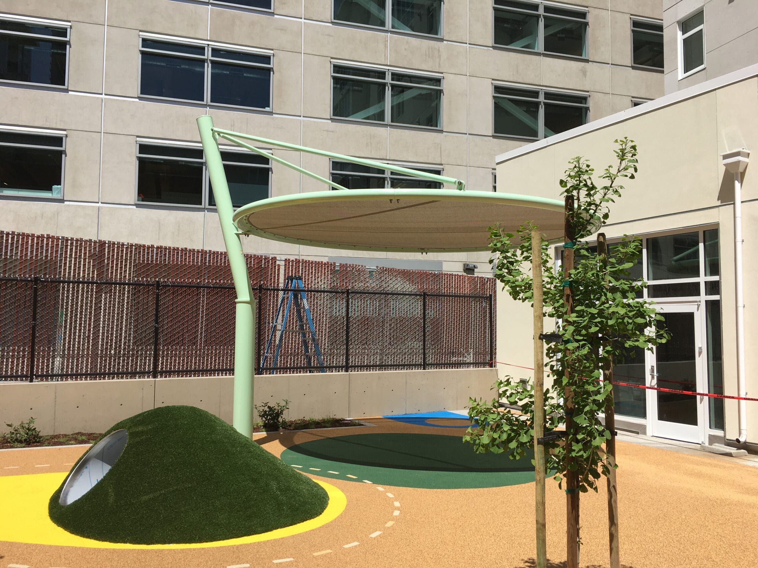 Minimalist cantilever circular fabric shade with pale green curved support over colorful playground surface
