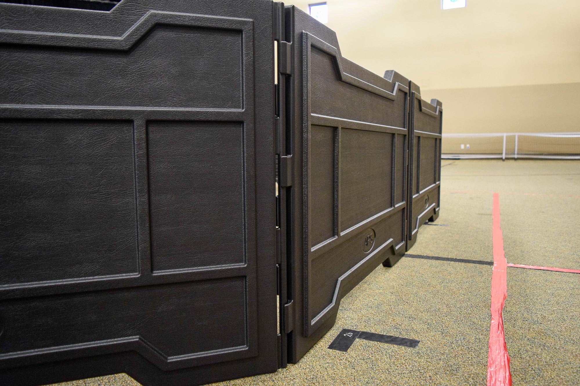 Portable black folding panels forming an indoor GaGa ball pit on carpet with red and black floor markings