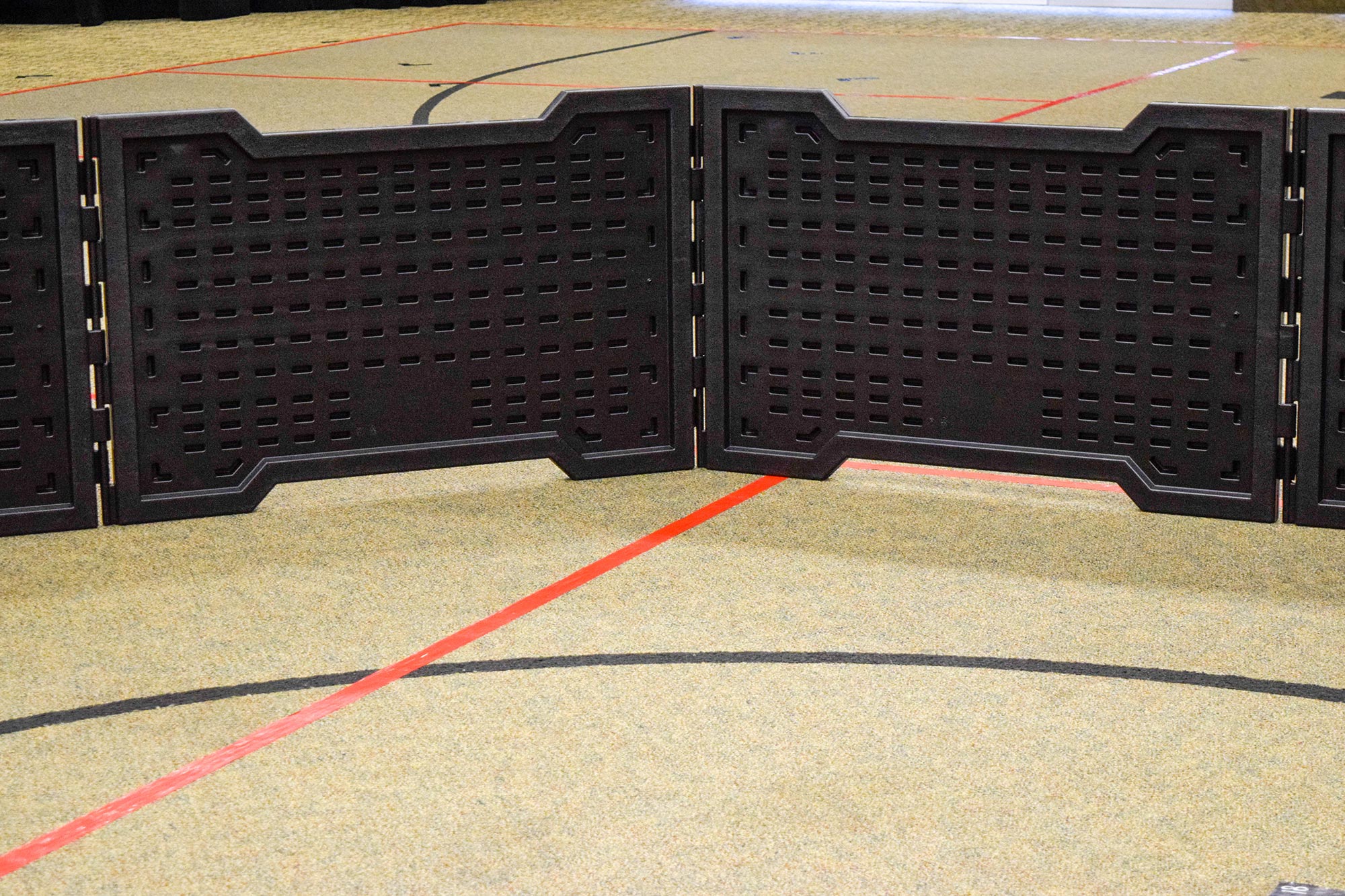 Portable black folding panels forming a modular indoor GaGa ball pit on a sports floor with red and black court lines