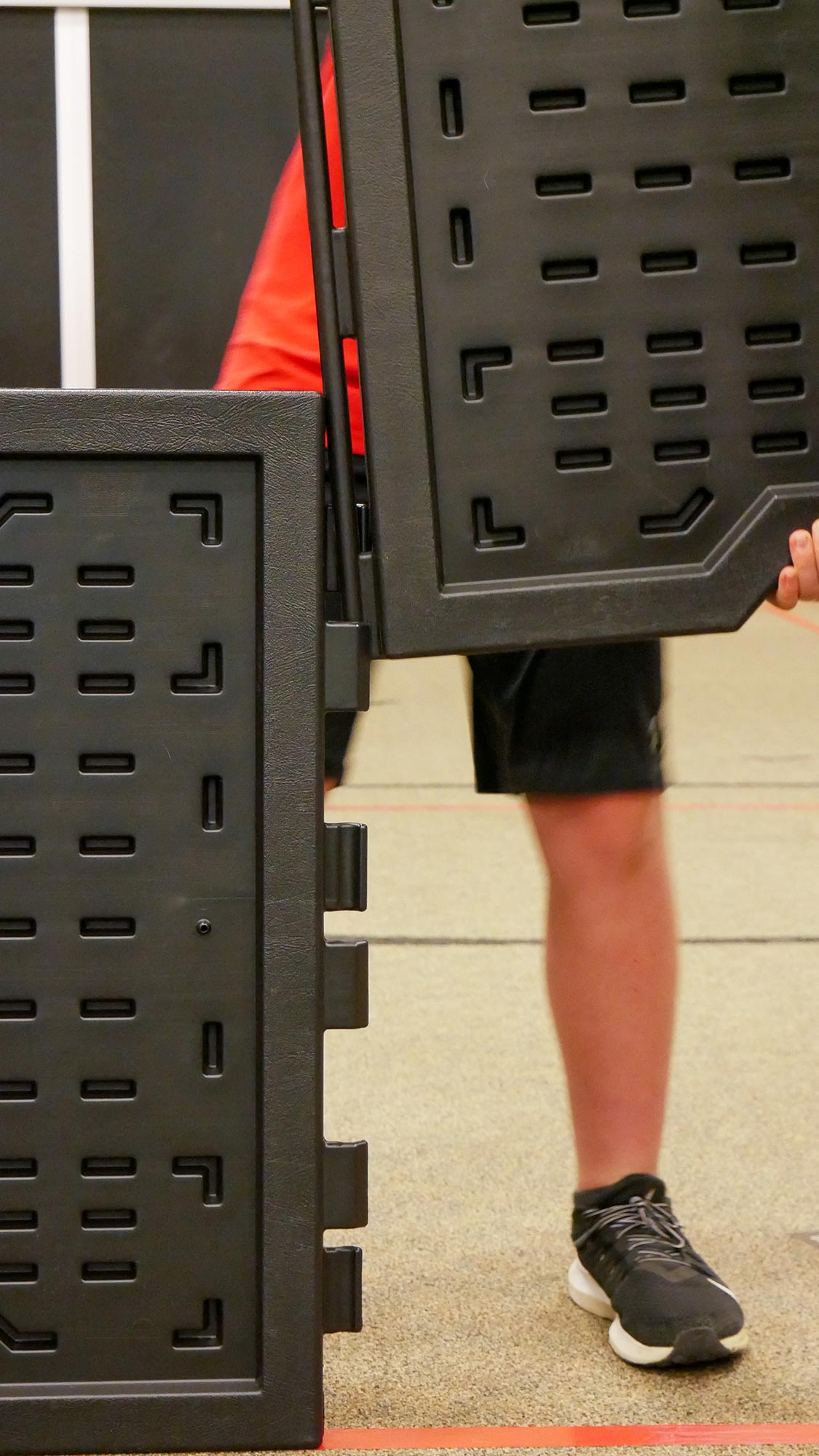 Black interlocking portable GaGa ball pit panels held by a person wearing black sneakers and red shirt