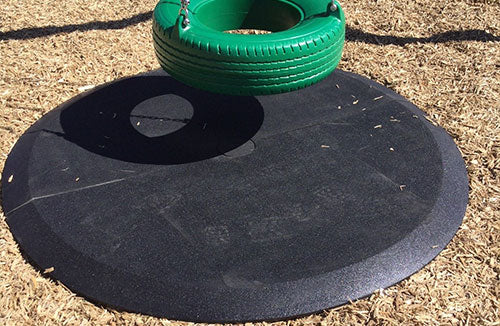 Black rubber playground wear mat with beveled edges beneath green tire swing on wood chip surfacing