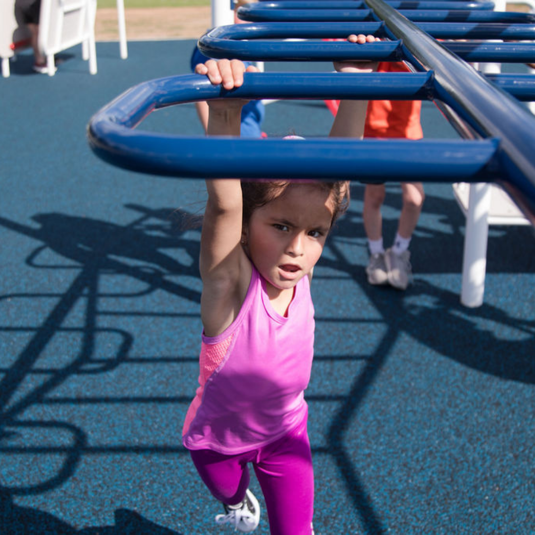 Child in pink activewear using blue outdoor strength training bars on playground surface