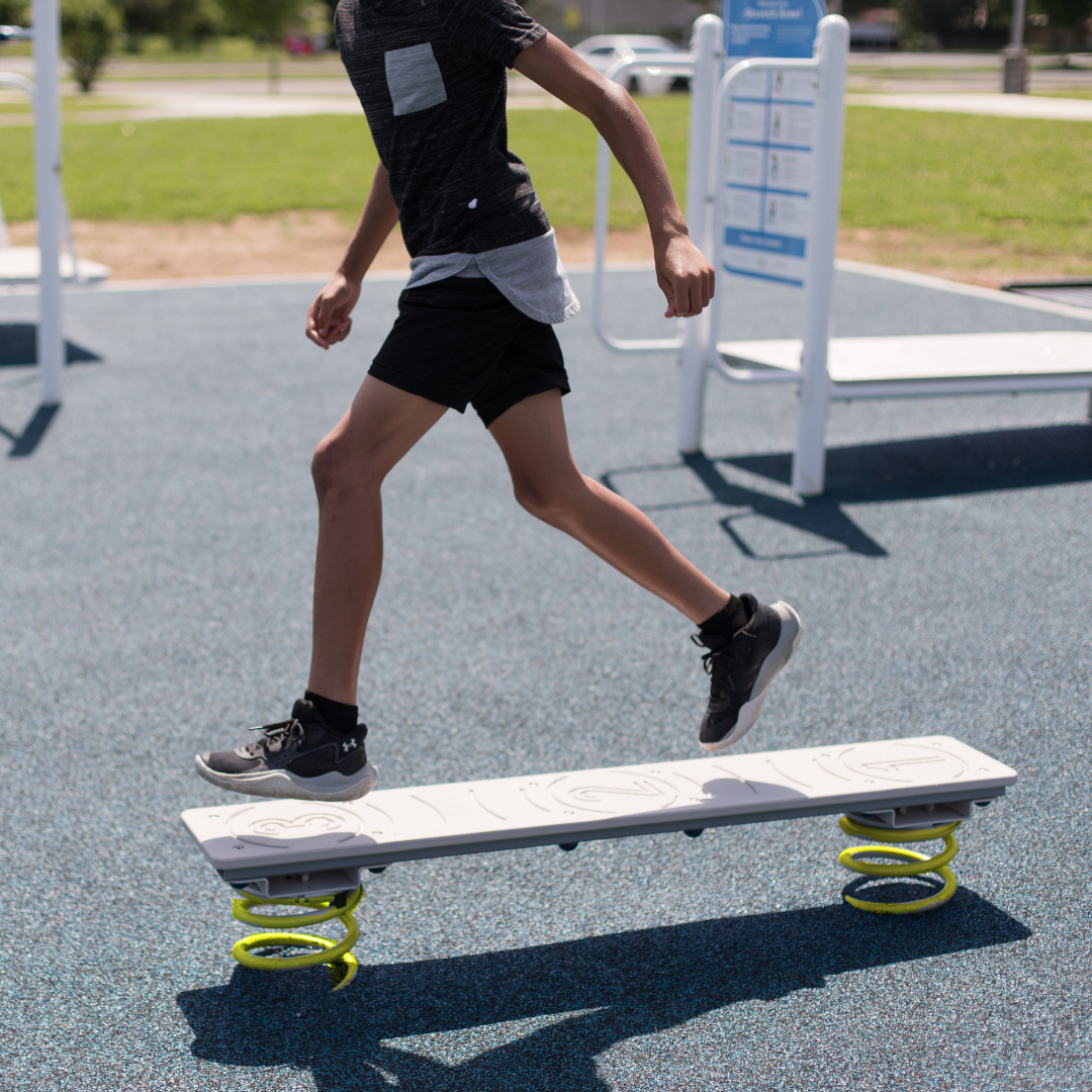 Child balancing on spring-mounted outdoor balance board with textured surface and numbered stepping zones