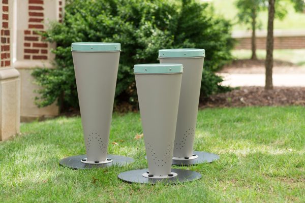 Three taupe synthetic-headed outdoor percussion drums with powder-coated steel bodies on grass in a park setting
