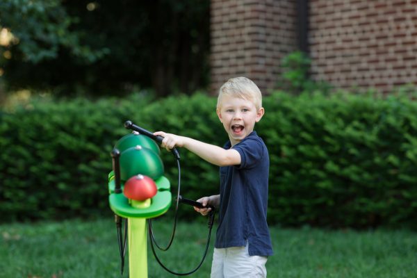 Child playing on a green caterpillar-shaped outdoor musical instrument with colorful bells in a garden setting