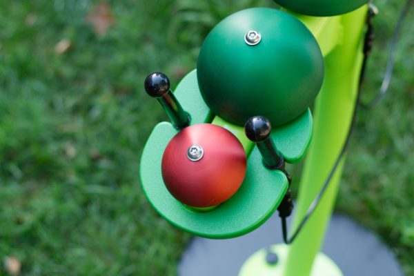 Colorful caterpillar-shaped outdoor musical playground instrument with green and red bells and black mallets on grass