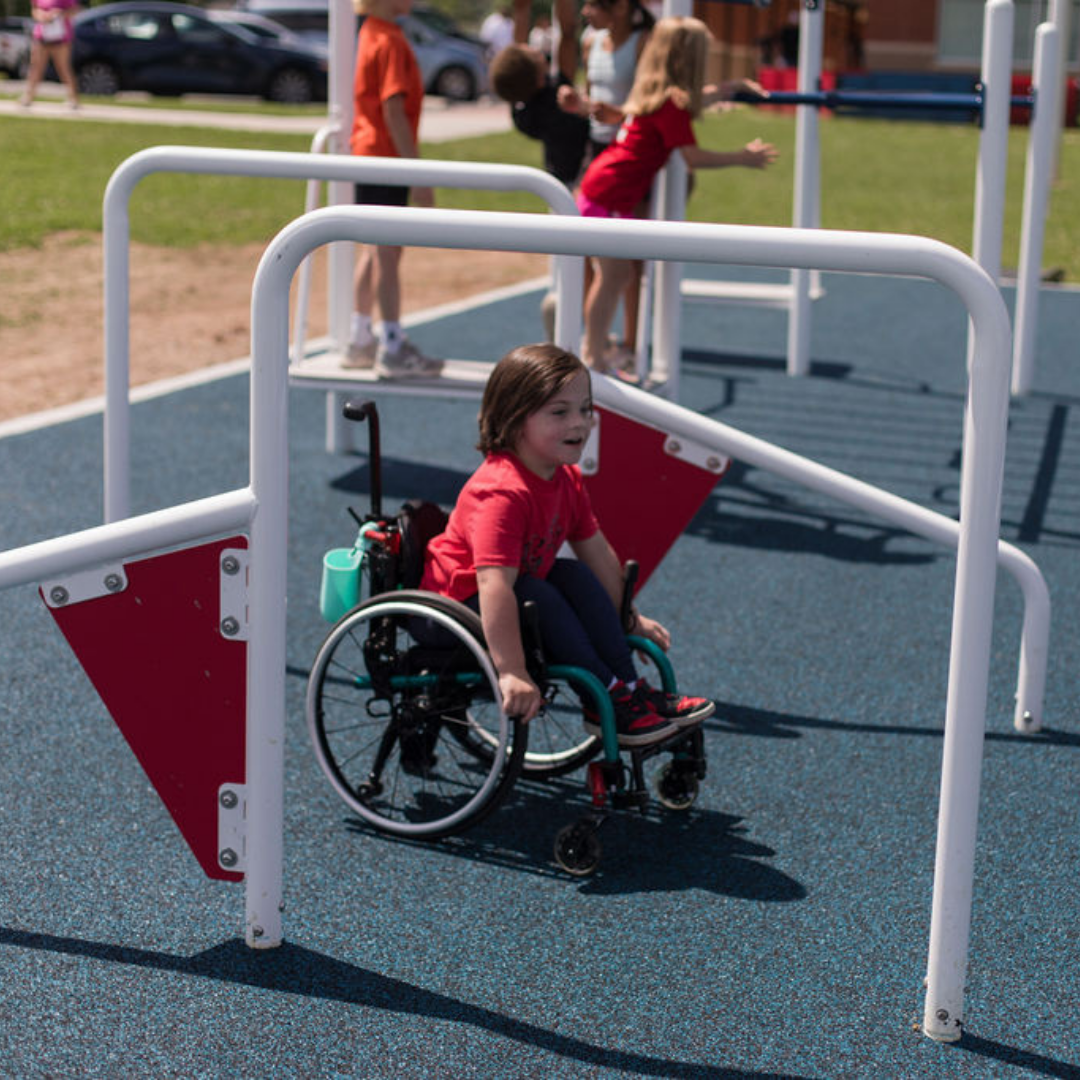 Child in wheelchair navigating accessible outdoor fitness challenge bars on blue safety surface with other children nearby