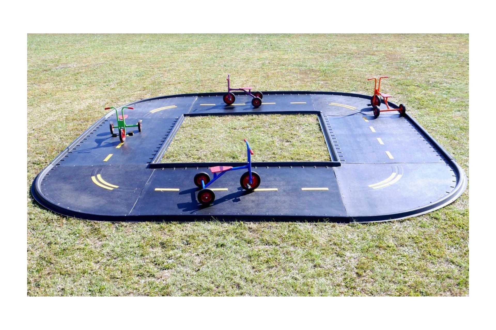 Outdoor black modular trike path with yellow road markings and four colorful tricycles on grass, designed for active play and coordination