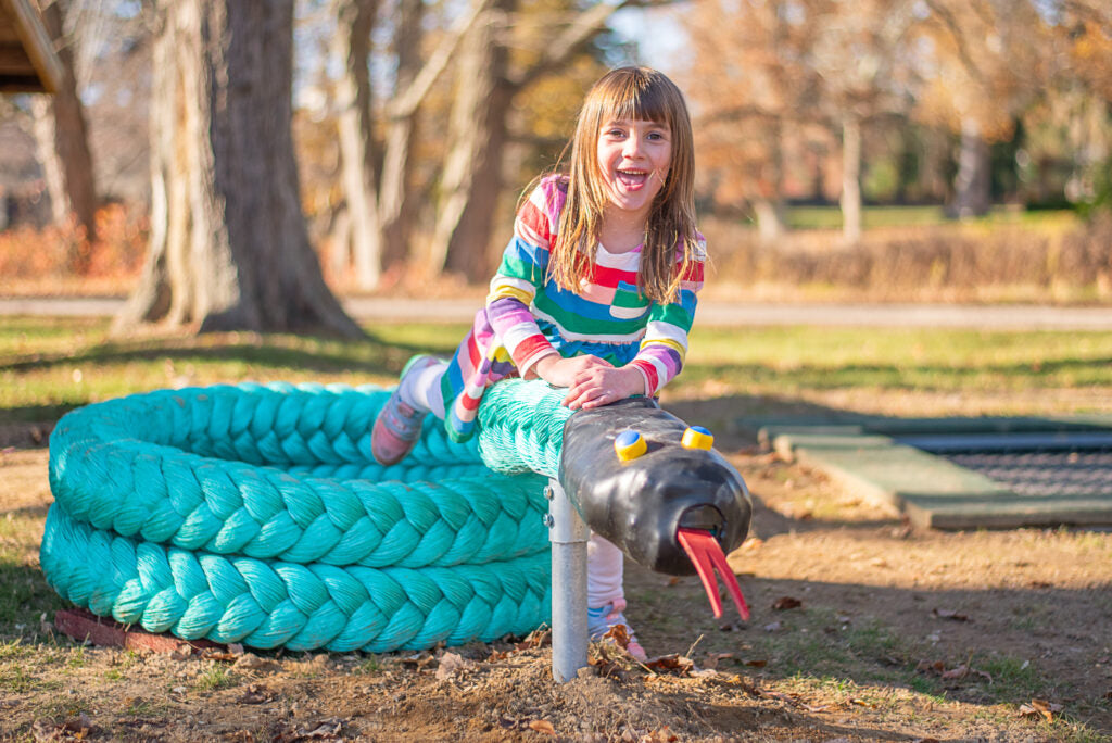 Child climbing on a turquoise snake-shaped play structure with textured coils, black head, yellow eyes, and red tongue