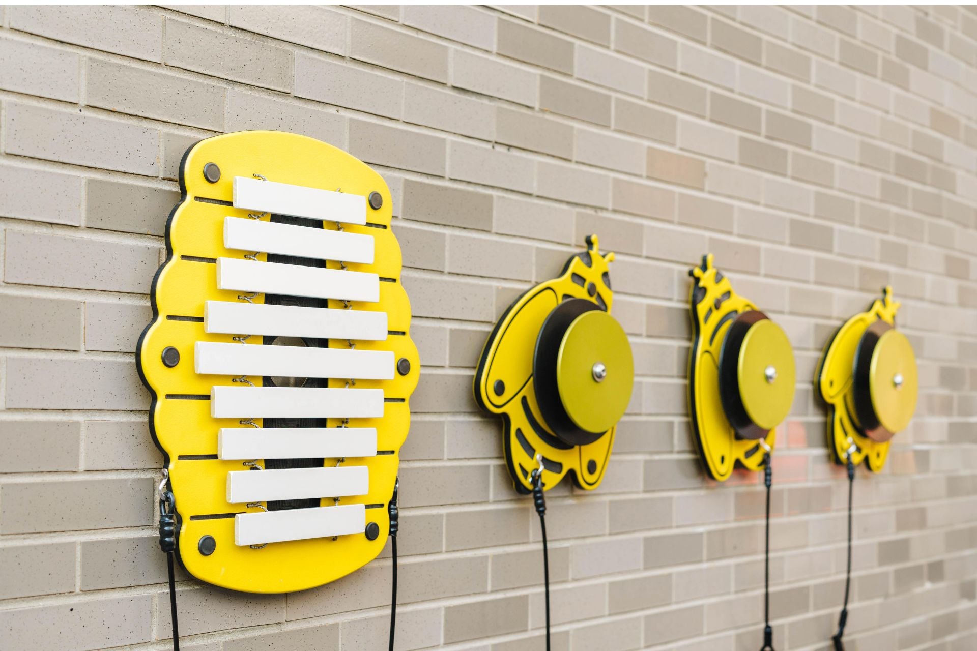 Yellow honeycomb-shaped metallophone with white bars and three bee-shaped yellow percussion instruments mounted on a brick wall