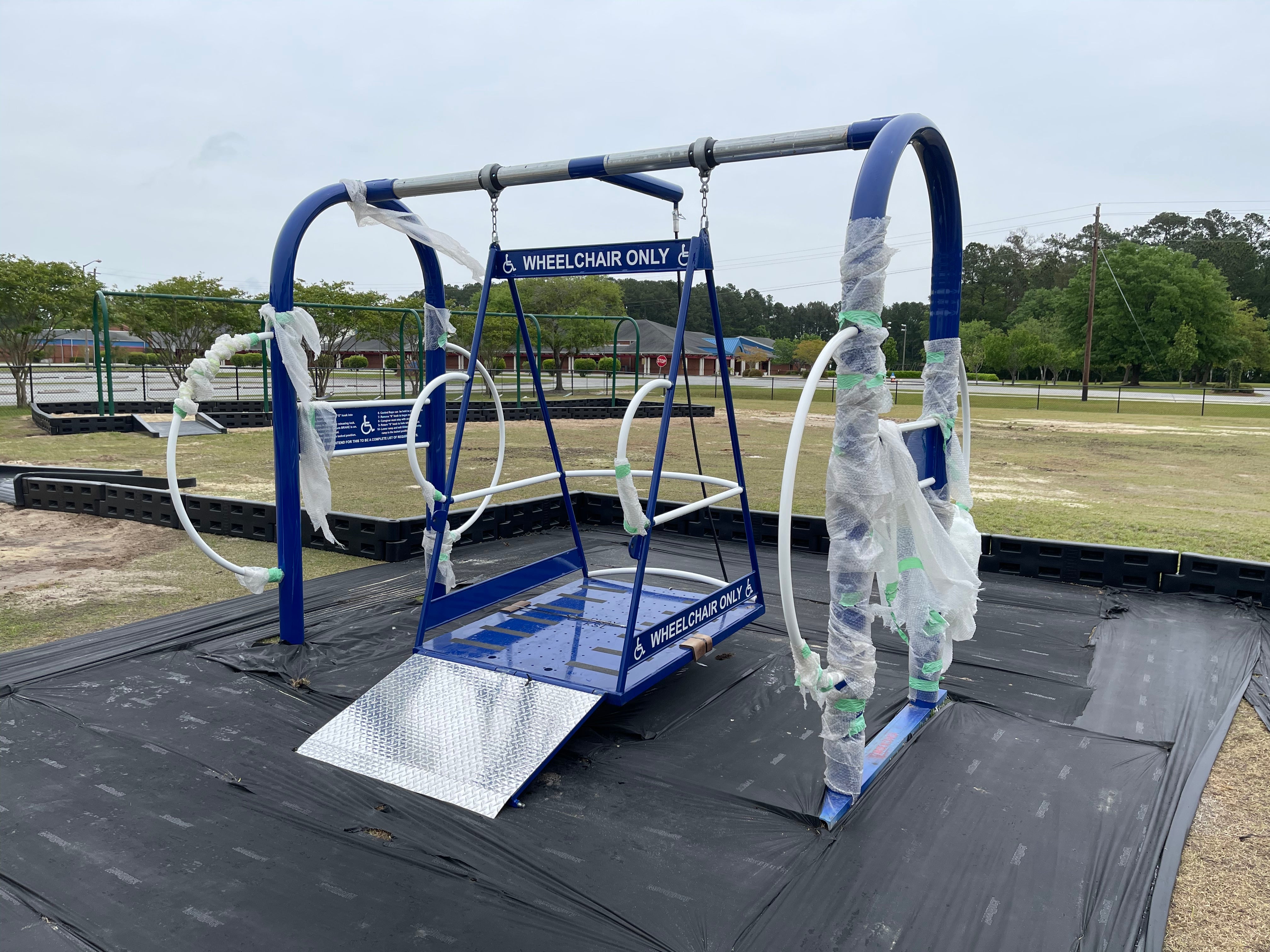Blue commercial wheelchair-accessible swing set with ramp, safety rings, and designated wheelchair-only play area markings