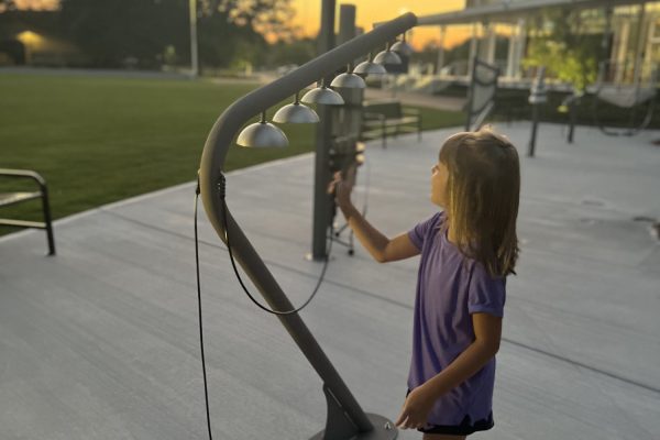 Child playing a sleek outdoor musical instrument with seven metal bells on a curved frame in a park setting