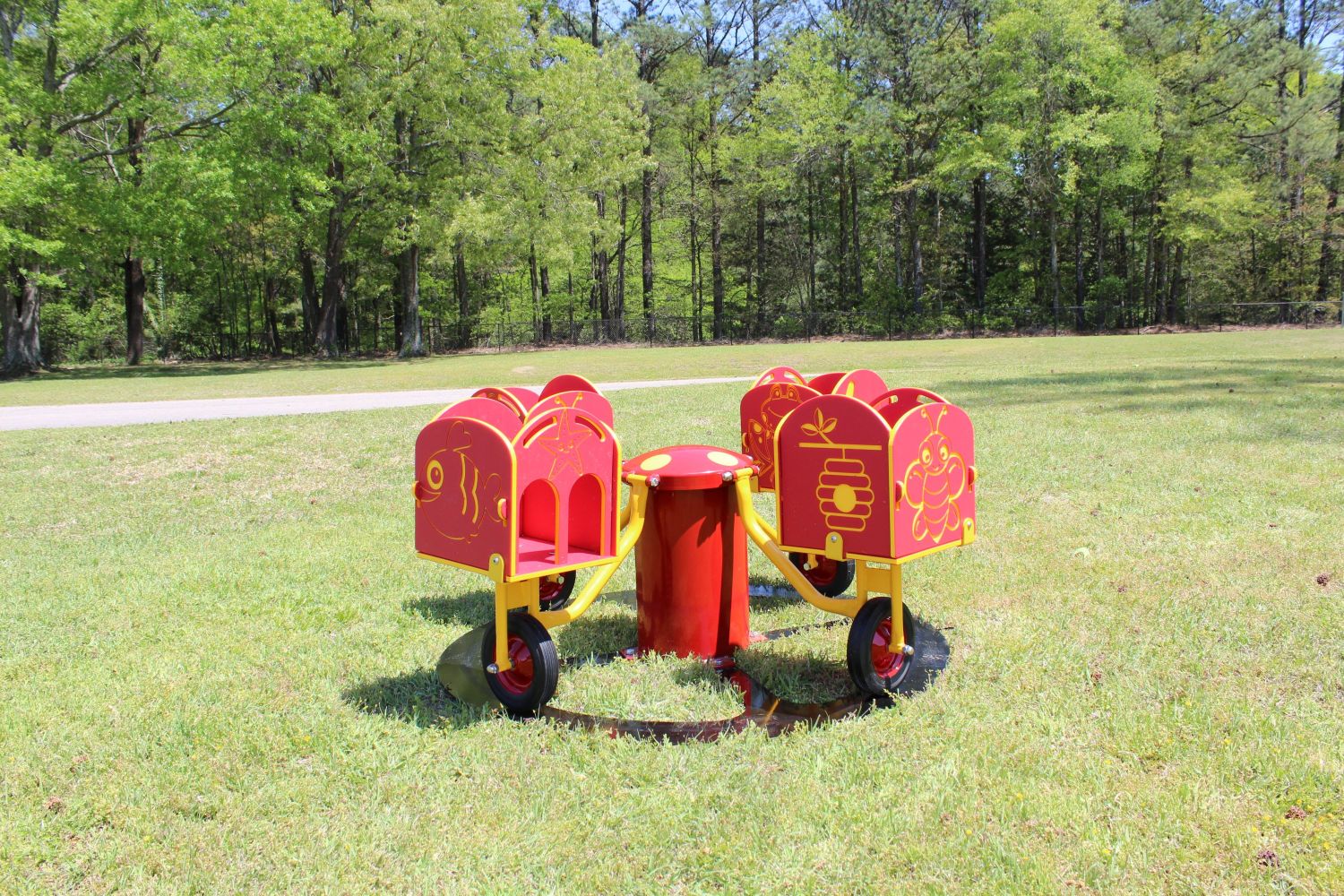 Carrington's Carousel four-seat red and yellow merry-go-round with playful animal and nature designs on grassy playground