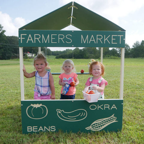 Farmers Market Playhouse with three toddlers playing inside, green panels featuring vegetable illustrations and labels.