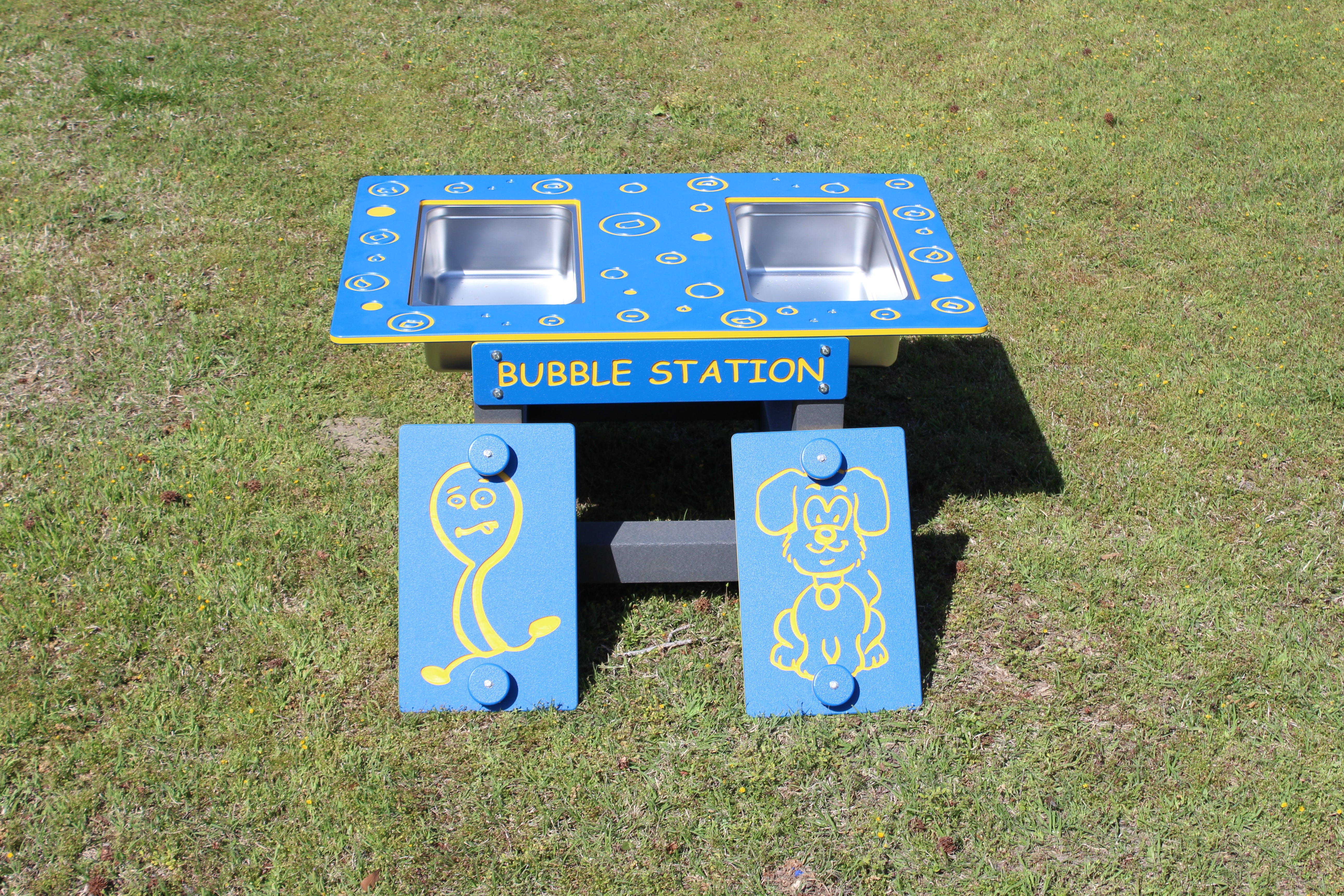 Blue and yellow outdoor bubble play station with two stainless steel basins and cartoon character panels on grass
