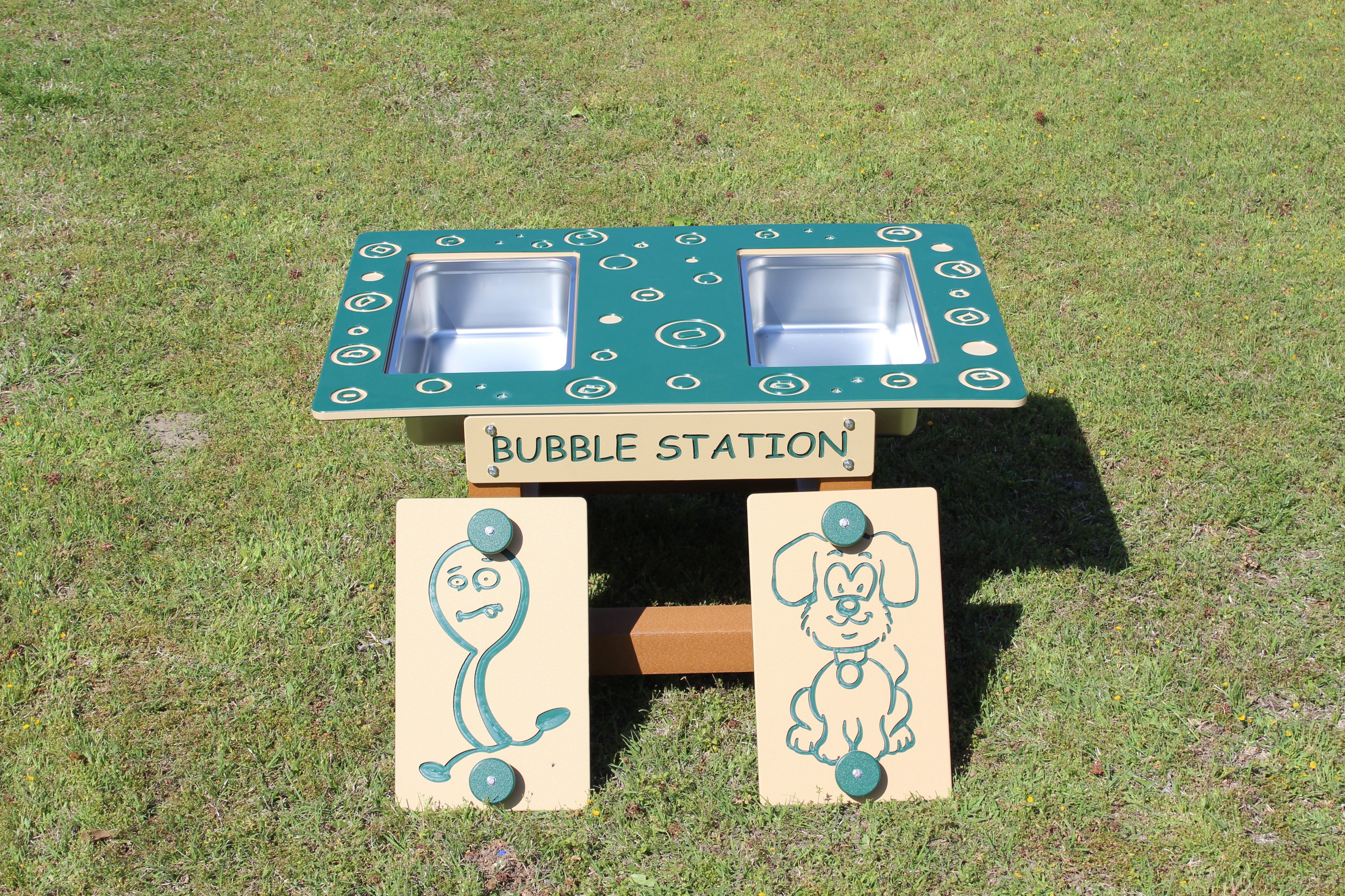 Outdoor green and tan bubble play station with two stainless steel basins and cartoon character panels on grass