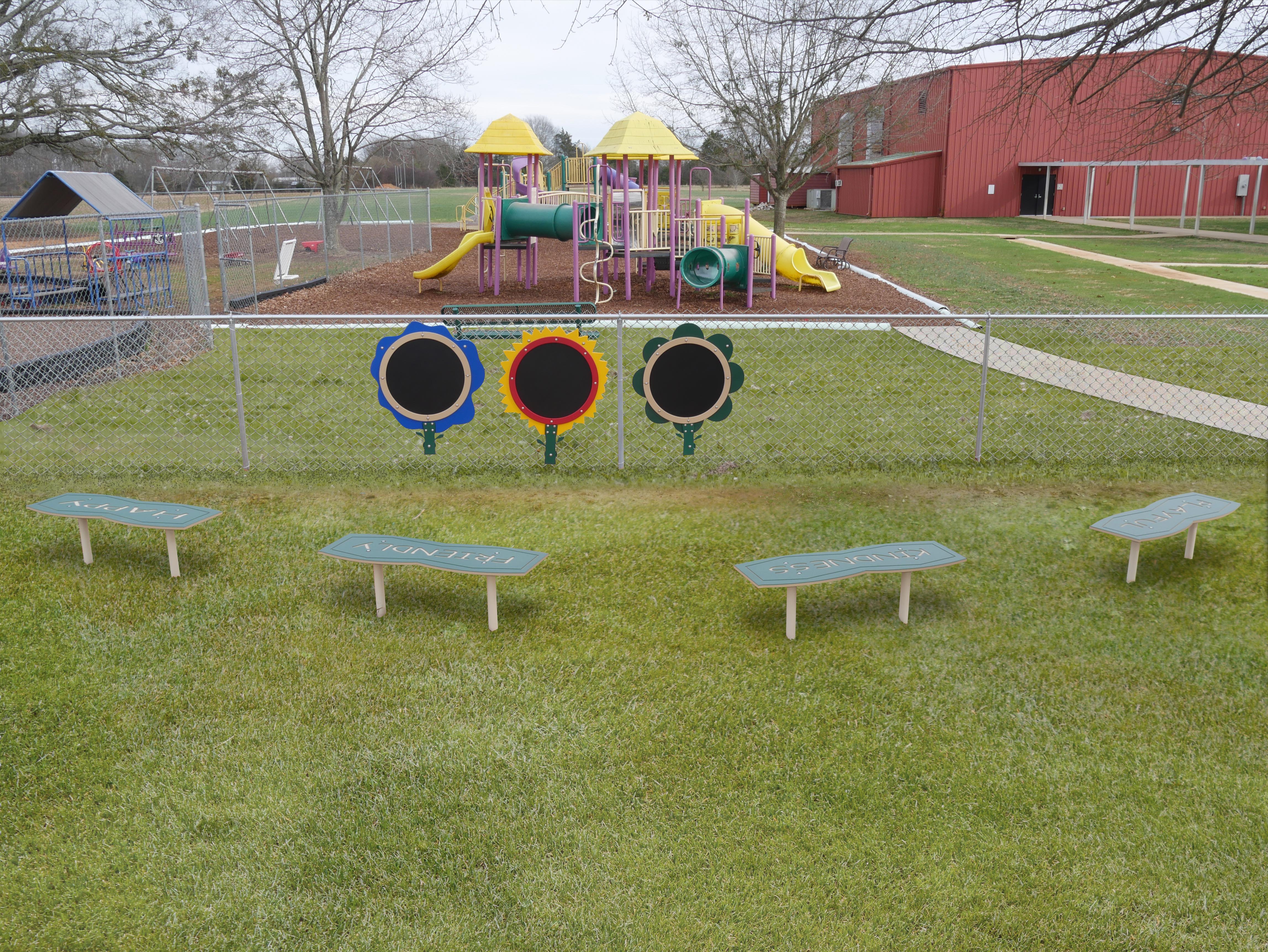 4-Foot Outdoor Character Bench on grass near playground with HAPPY, FRIENDLY, KINDNESS, and HONESTY designs