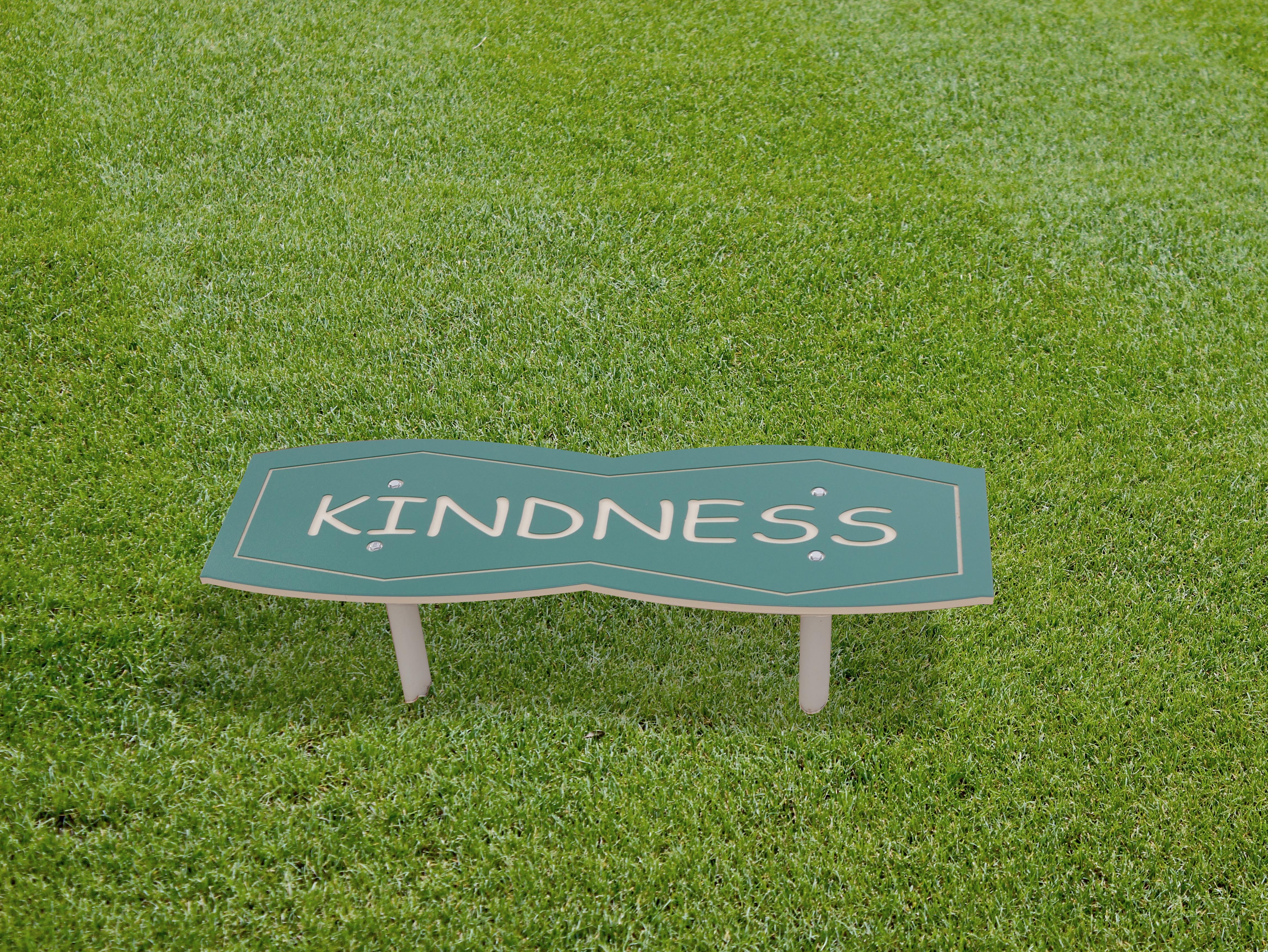 Green outdoor bench with smooth edges featuring playful childlike figures and a kindness message on grass