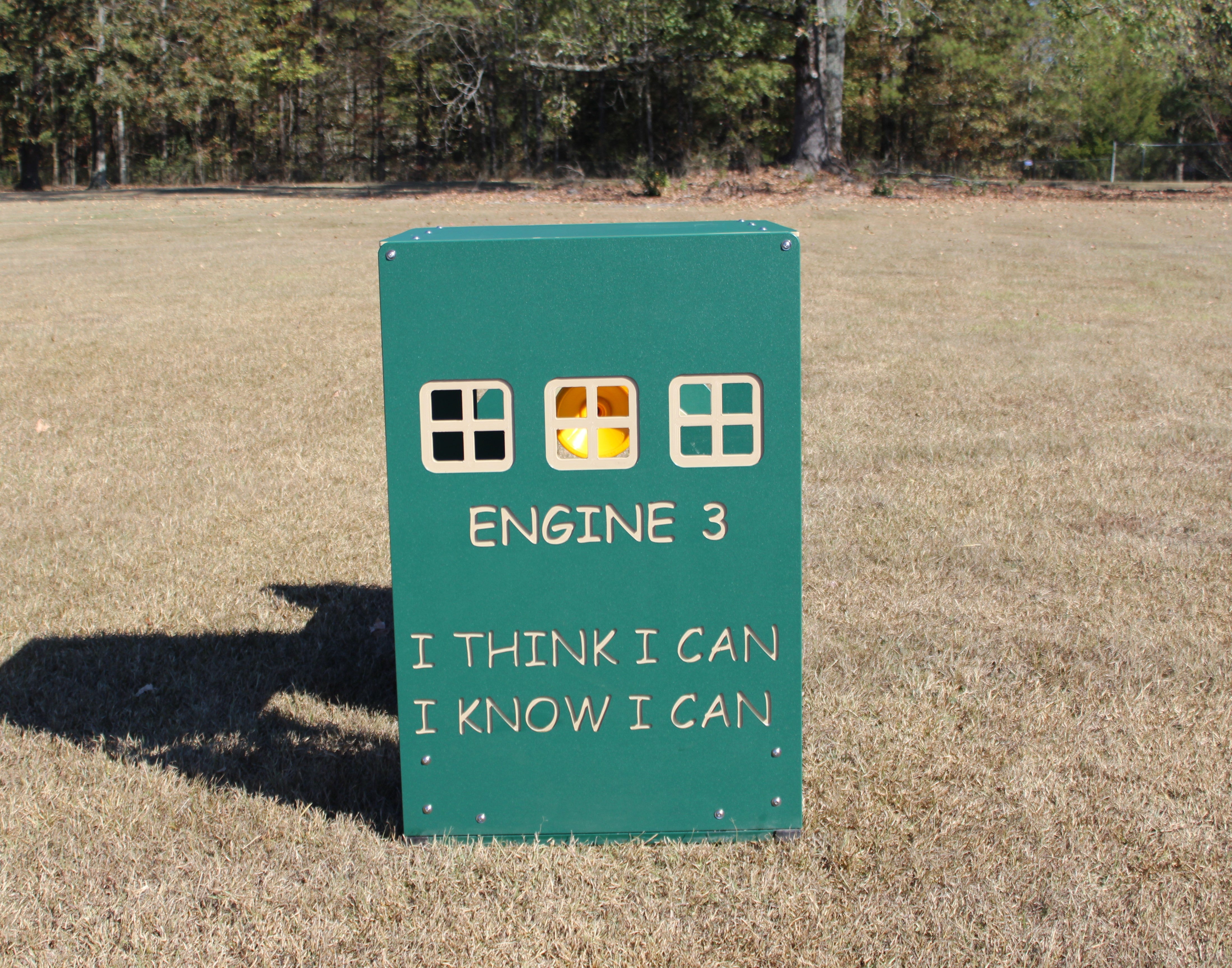 Green outdoor play structure shaped like a train engine with window cutouts and motivational text on grass