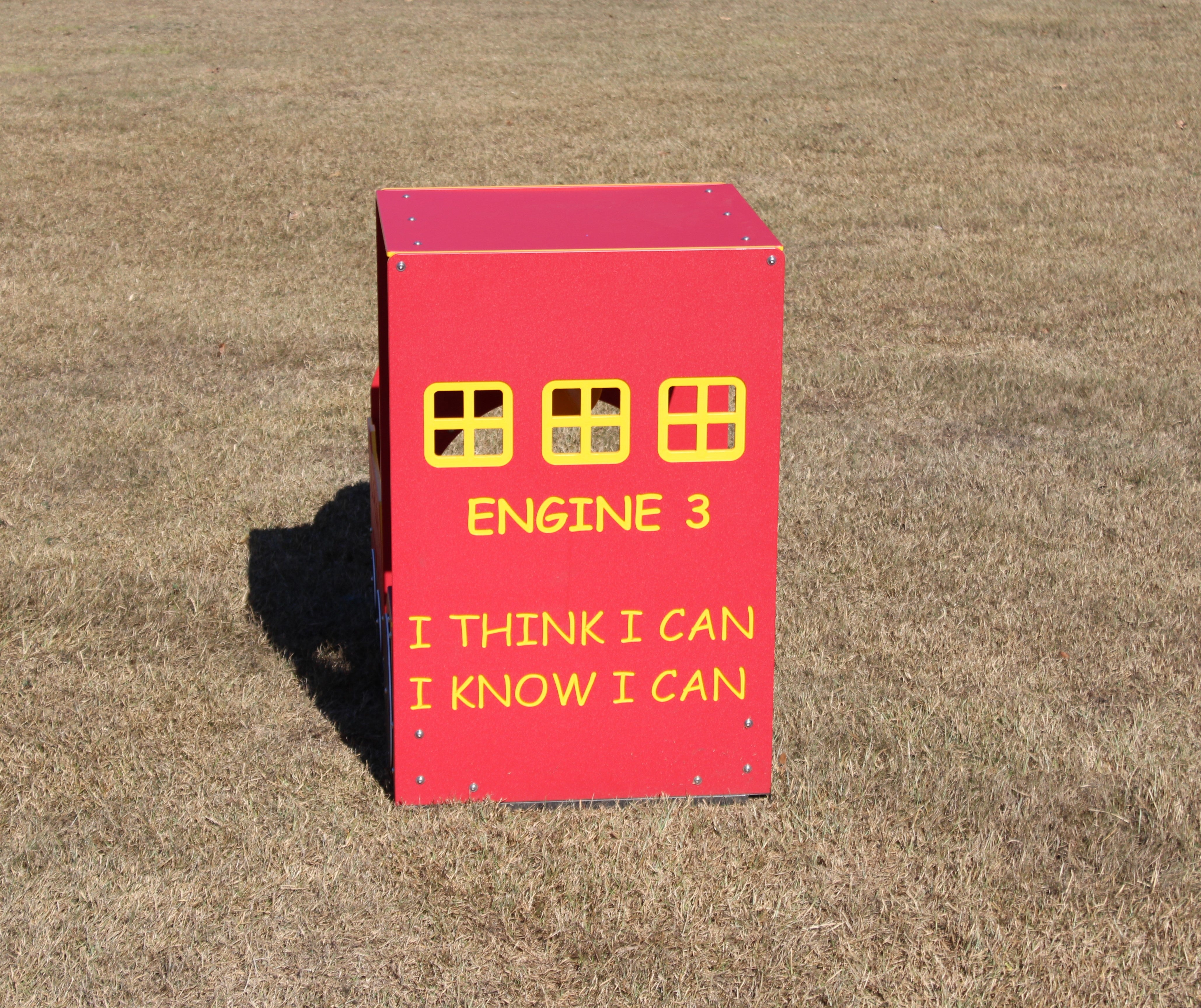 Red outdoor play structure shaped like a train engine with yellow window frames and motivational text on the side