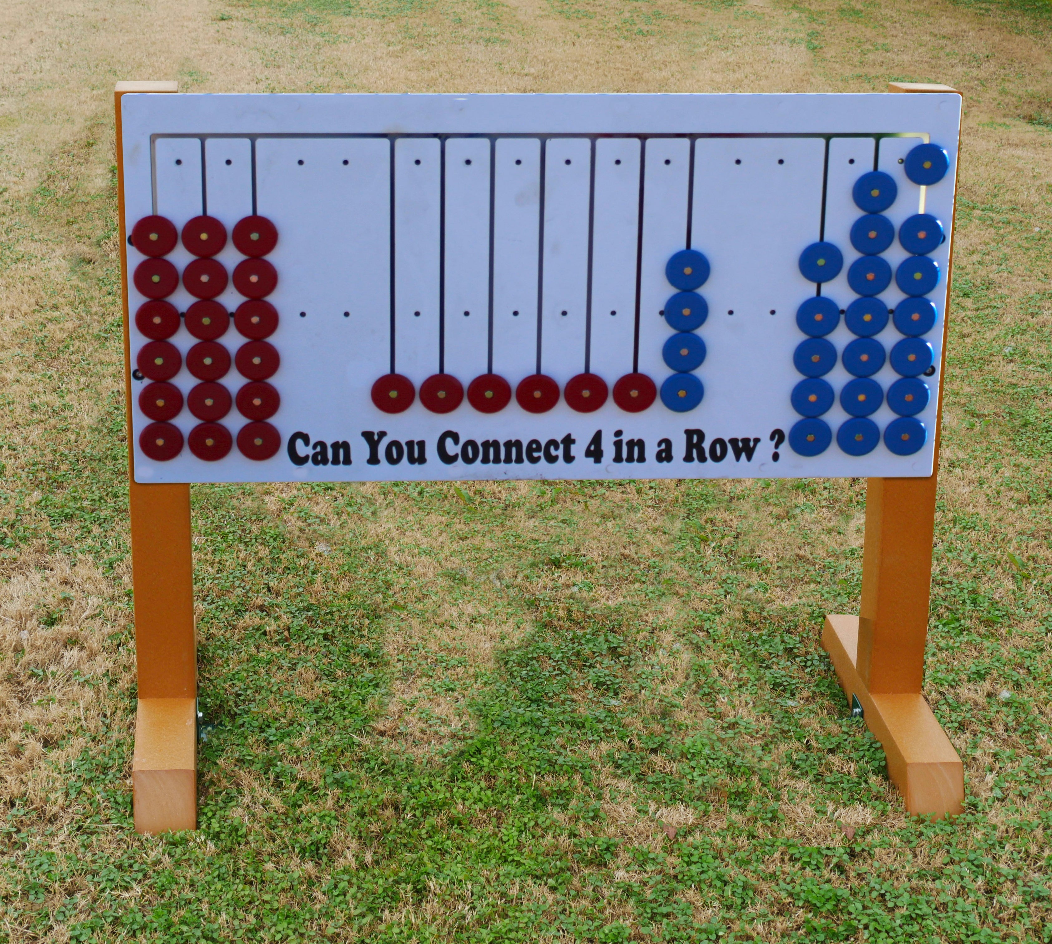 Outdoor Connect 4 game panel on legs with red and blue circular pieces arranged in vertical columns for playground use
