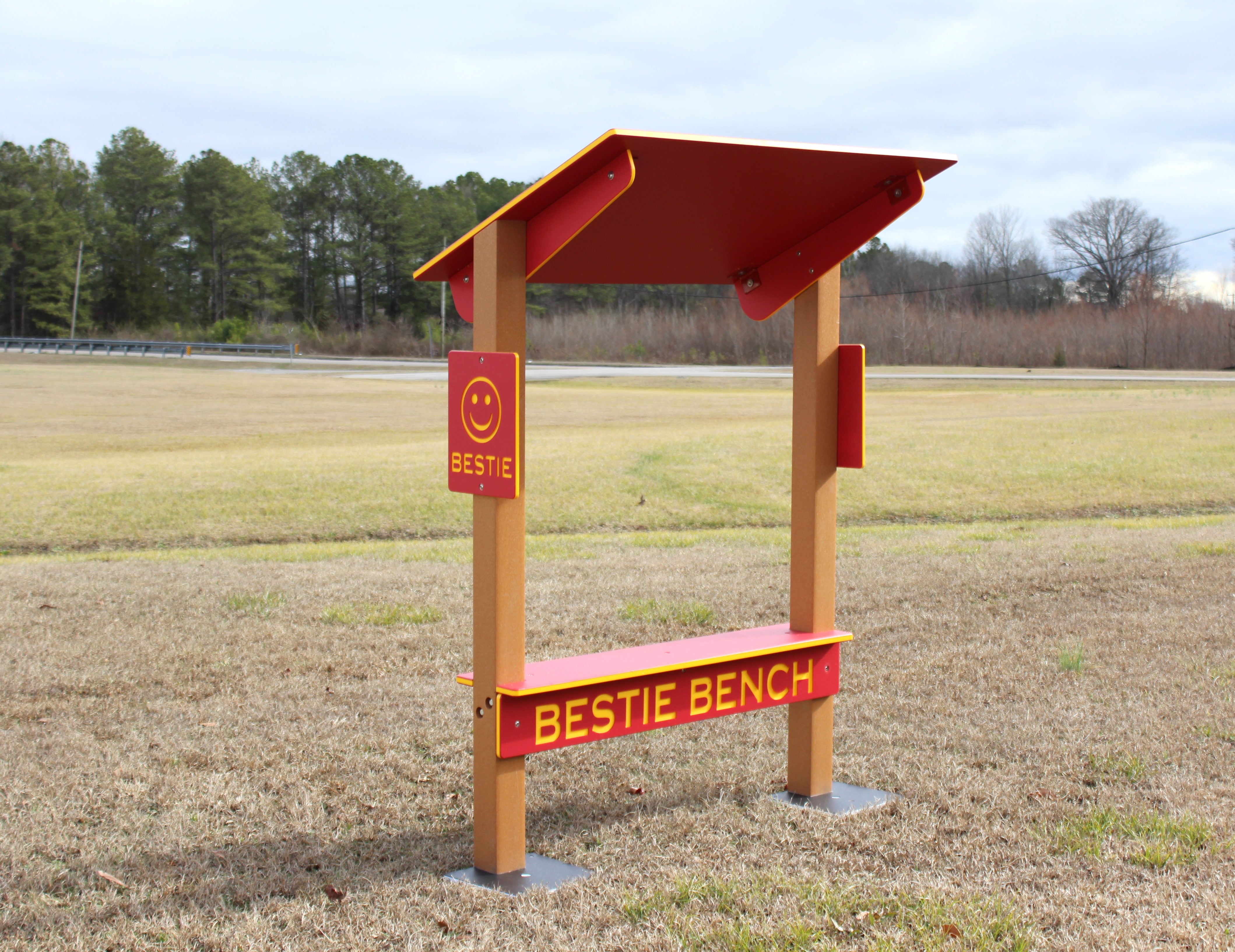 Red and yellow outdoor park bench with shade canopy and smiley face promoting friendship and inclusion