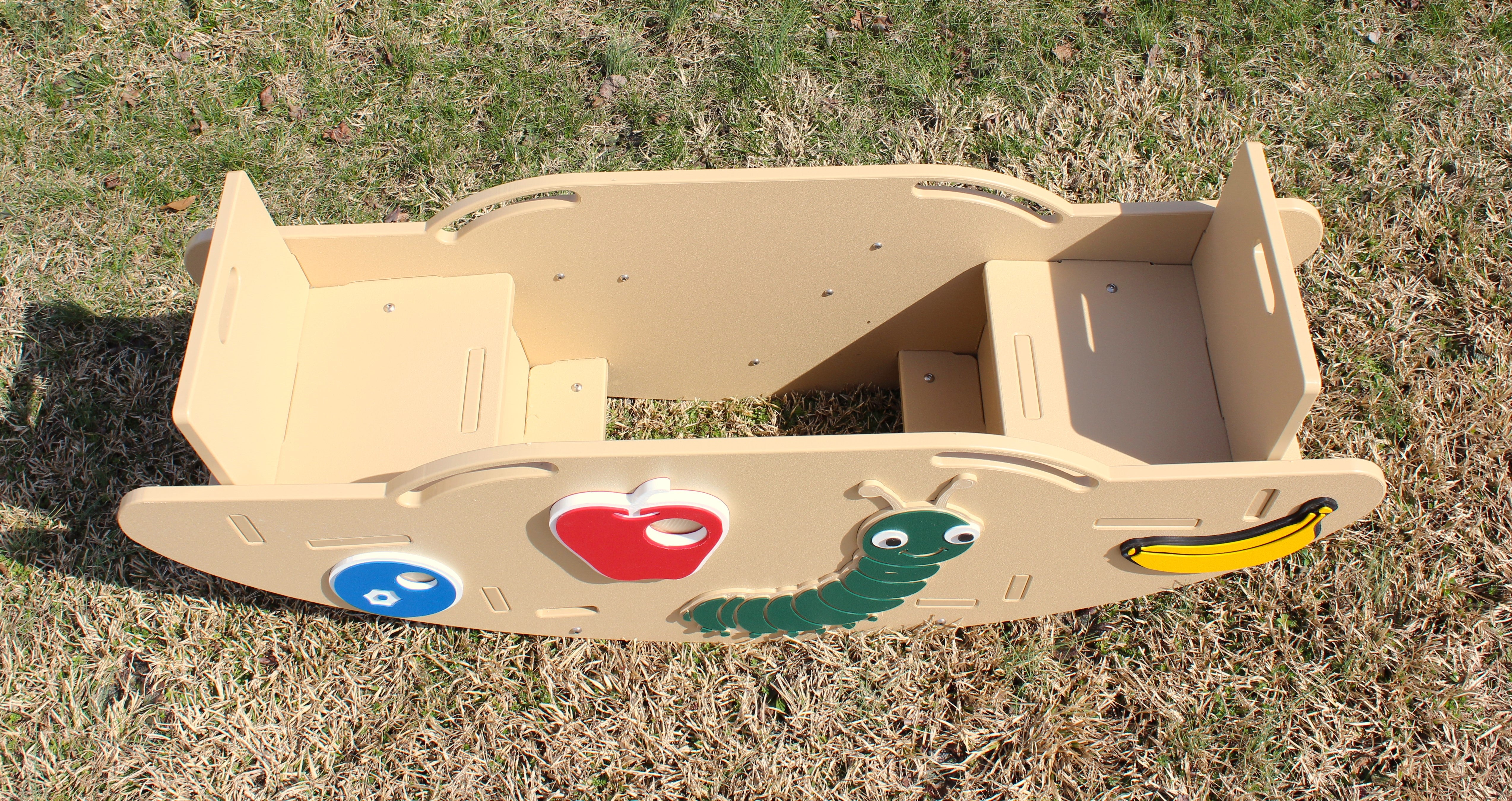 Overhead view of beige children's seesaw with colorful caterpillar and fruit figures, hand holds, and footrests on grass