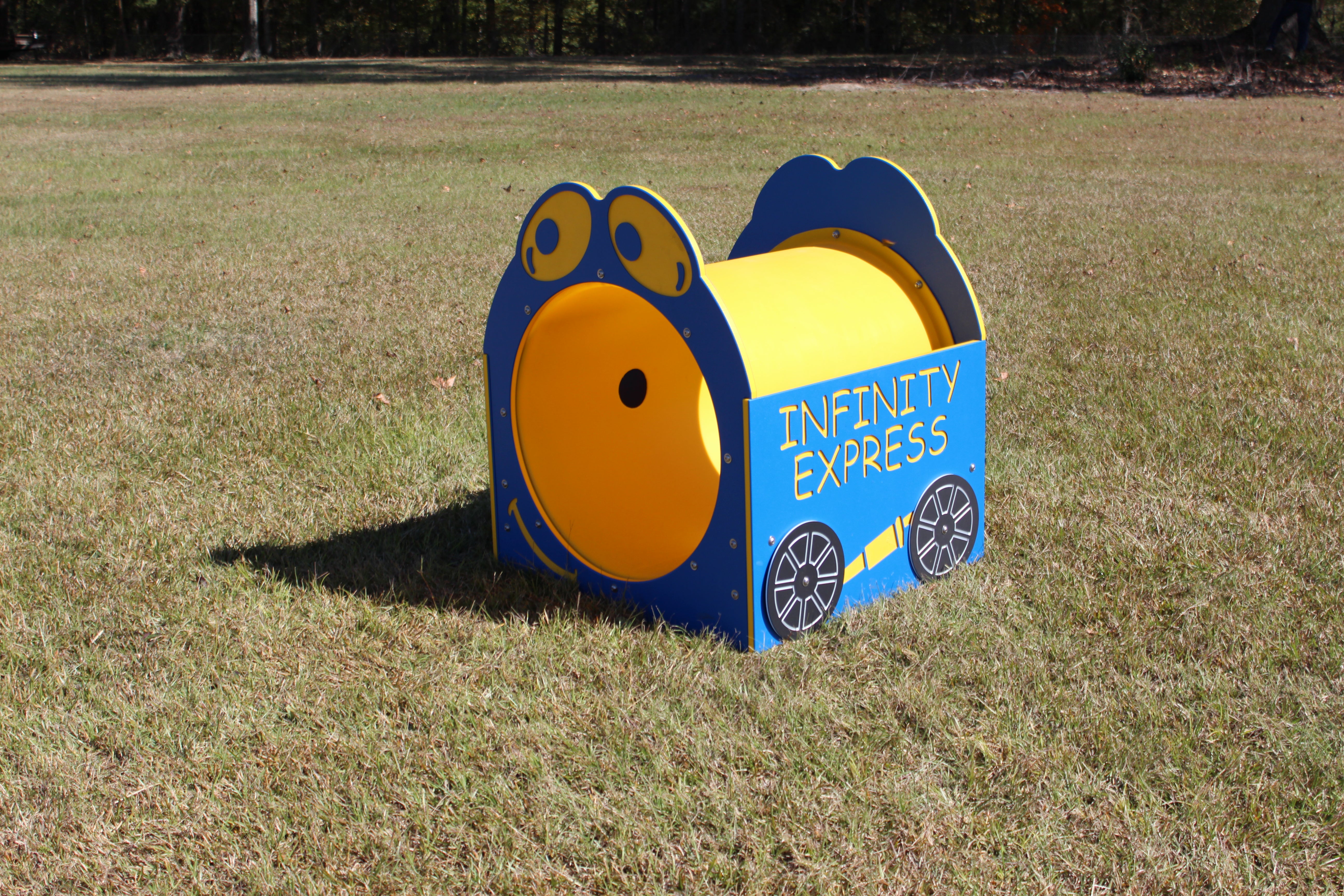 Infinity Express Tunnel playground climbing tunnel in bright yellow and blue with playful face and wheel designs on grass