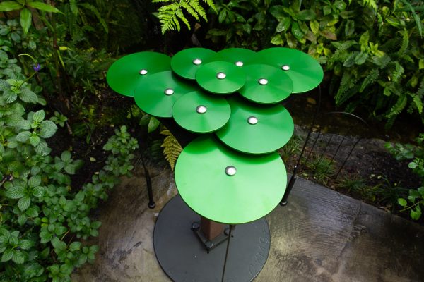 Overhead view of green anodized aluminum outdoor cymbals in layered clusters on metal stand, designed for interactive park play