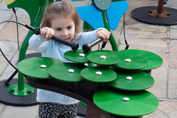 Child playing green outdoor musical cymbals with layered anodized aluminum discs and mallets in a park setting