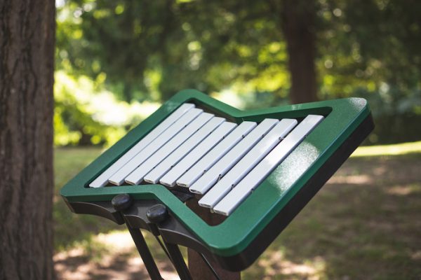Outdoor metallophone with nine silver aluminum bars in a green recycled plastic frame on black stands in a natural park setting