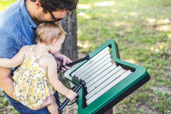Outdoor metallophone with green anodized aluminum bars, played by adult and child in park setting