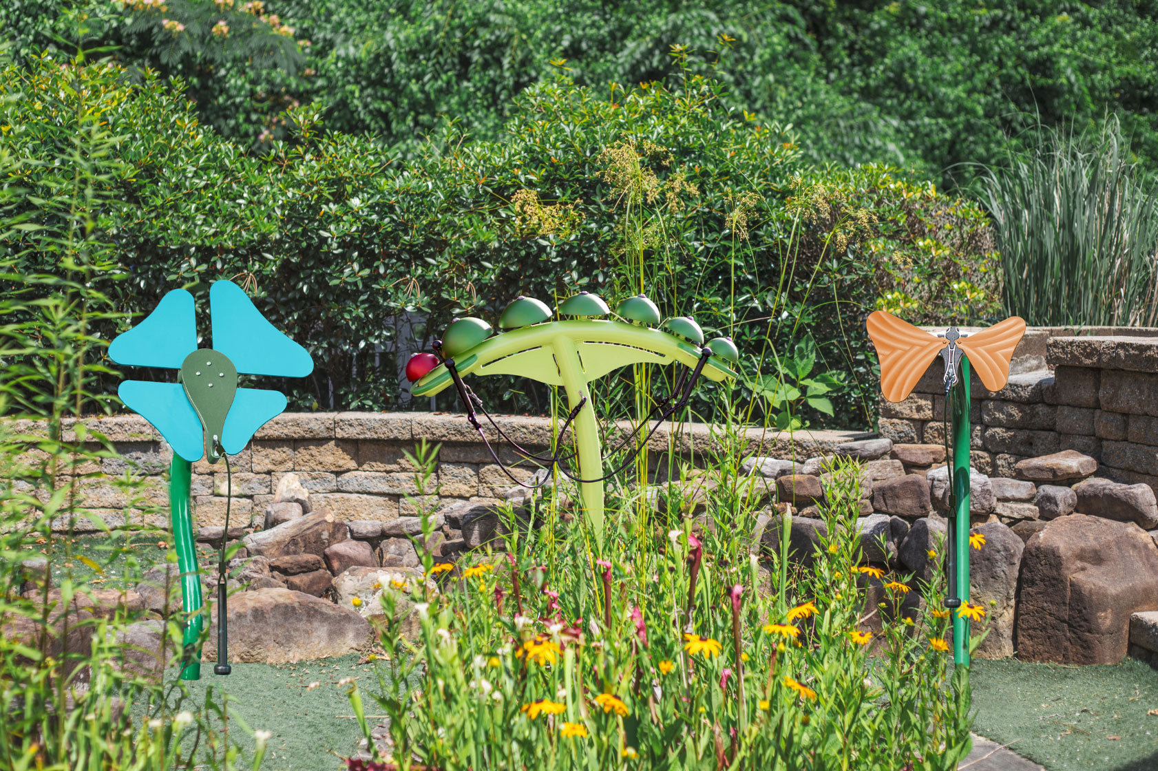 Colorful outdoor musical instruments shaped like a blue flower, green caterpillar arc, and orange butterfly among garden plants