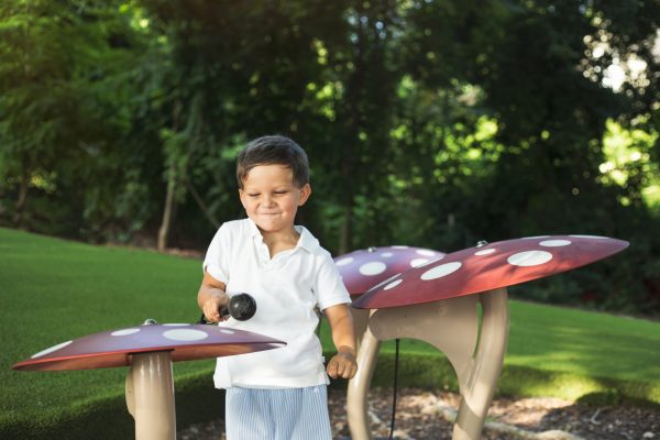 Child playing with red-capped outdoor musical mushrooms with white spots in a green garden setting