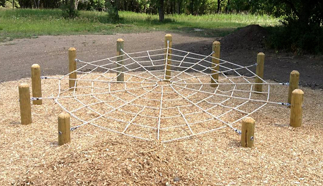 Outdoor spider web climbing net suspended between wooden posts over wood chip ground cover