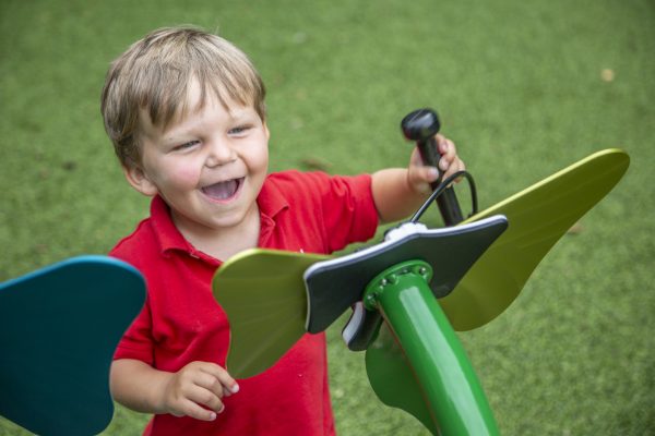 Toddler playing vibrant green and blue butterfly-shaped outdoor musical instruments with mallet on artificial grass