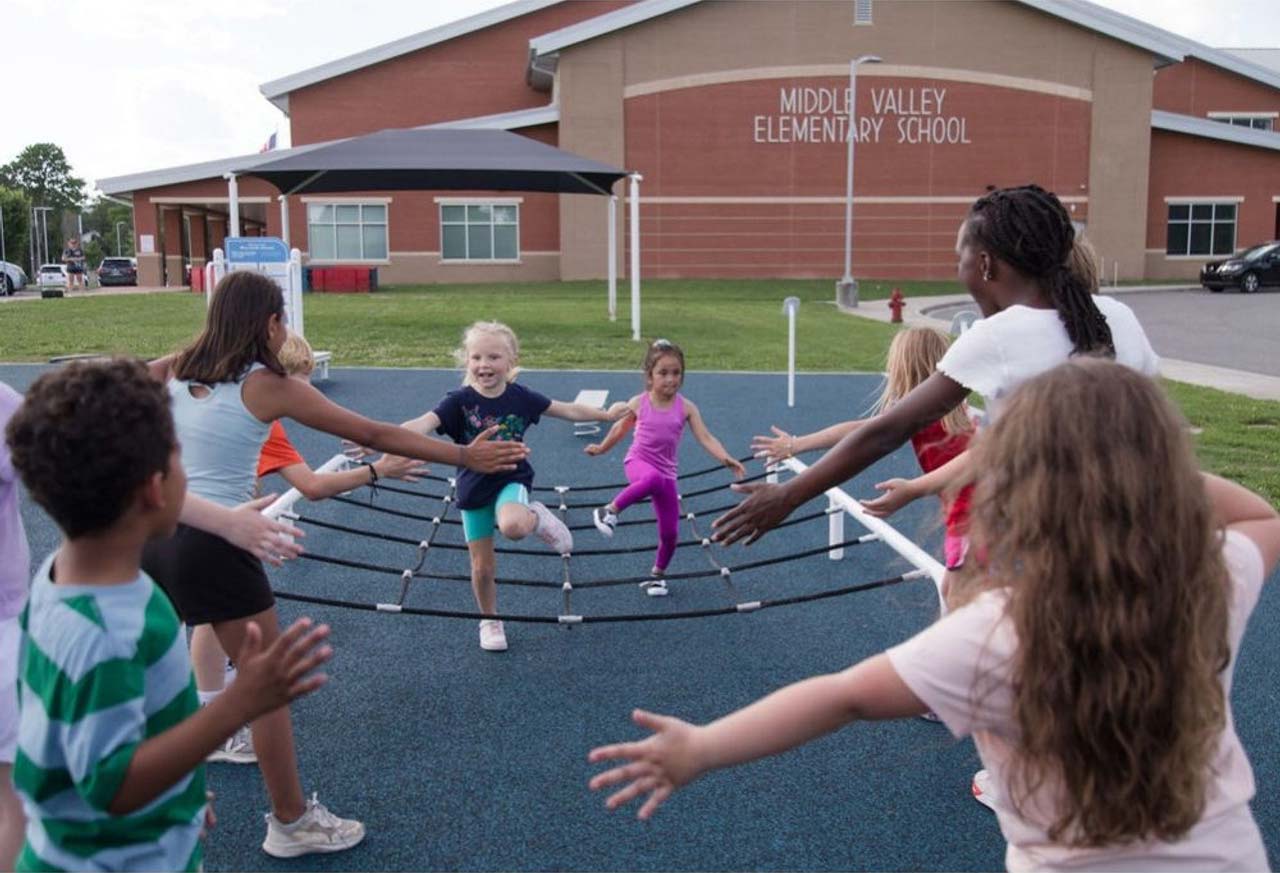 Children racing and cheering on a netted step zone on outdoor playground fitness equipment
