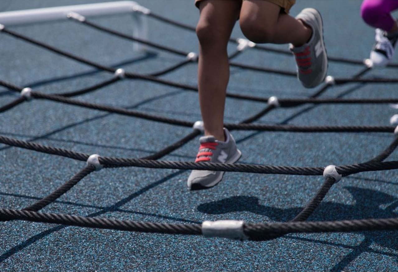 Child's foot on black rope netting of outdoor kids fitness step zone on blue surface