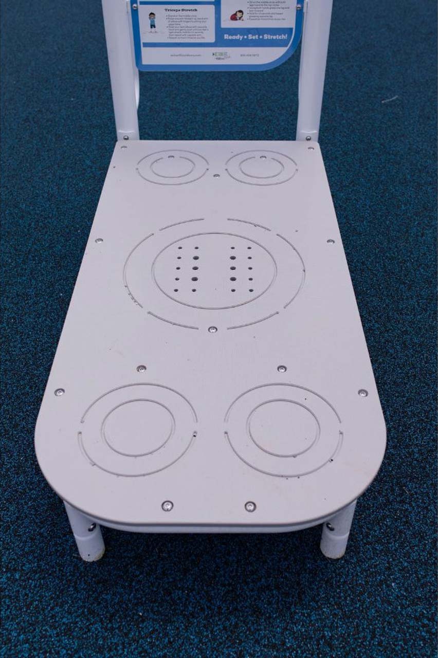 Outdoor kids fitness stretch station with circular foot and hand placement guides on textured blue surface