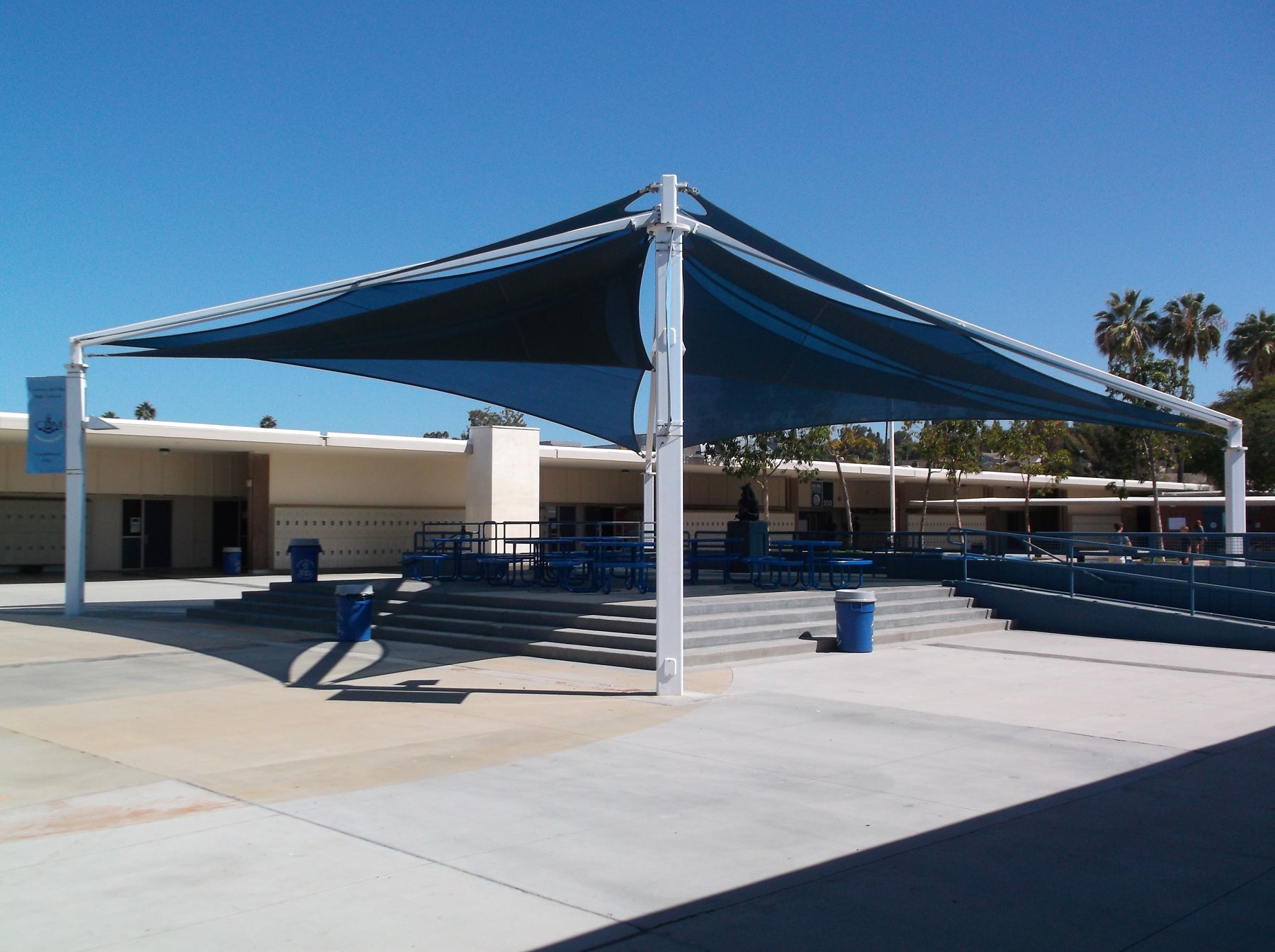 SuperSpan Multi-Layer Multi-Panel Shade Structure with blue fabric panels and white steel frame over outdoor school seating area