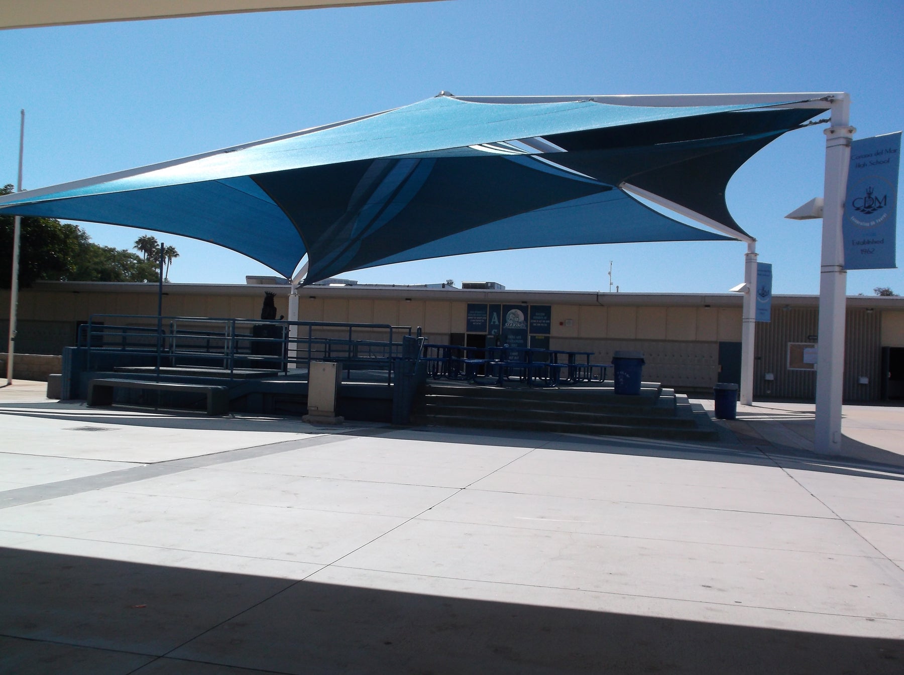 Blue multi-layer fabric shade structure with steel frame covering outdoor school courtyard seating area