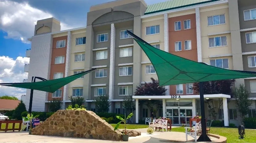 Black steel posts supporting green triangular shade sails over outdoor seating in front of a multi-story building
