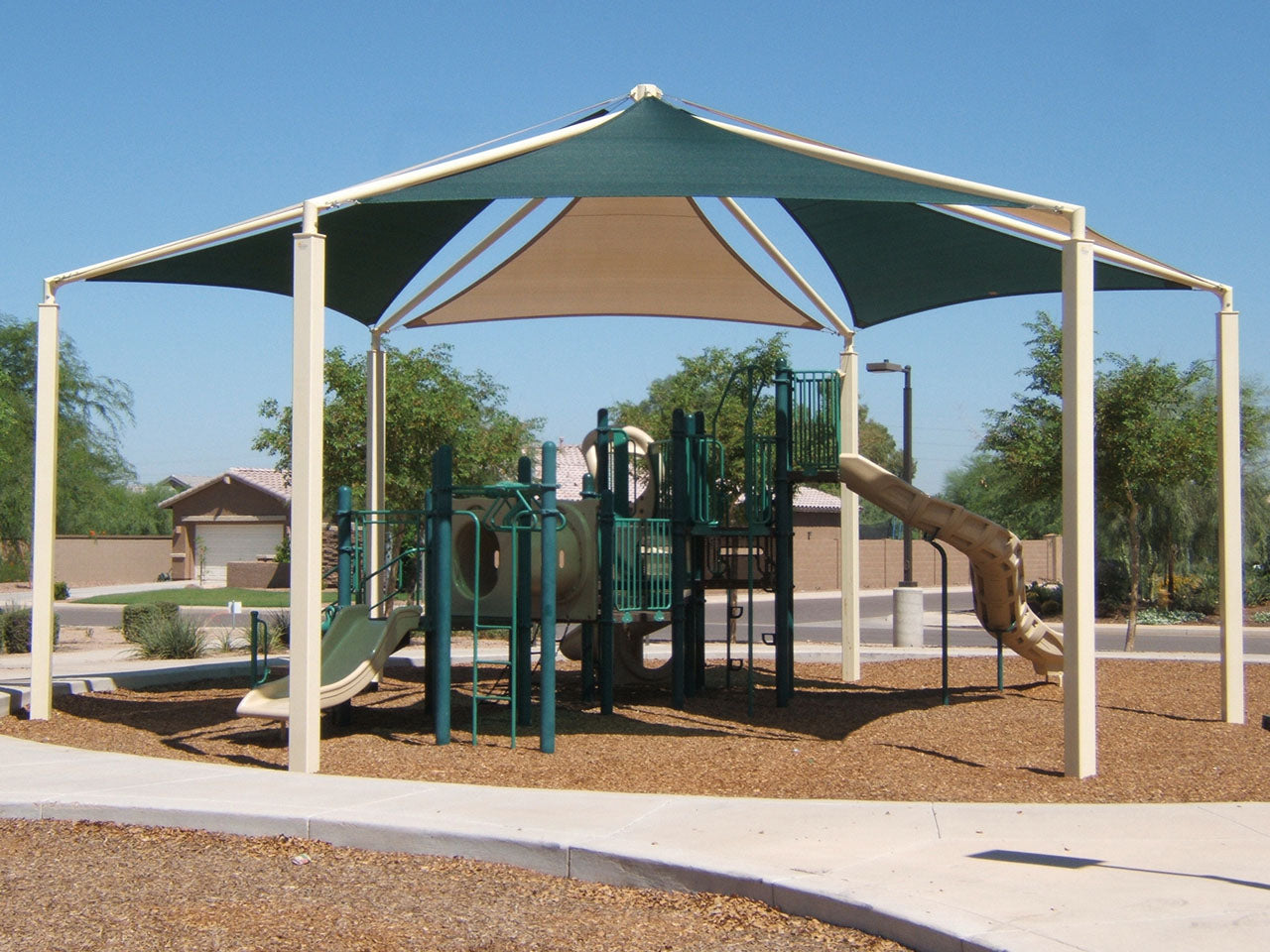 Hexagon Multi-panel Shade Structure with beige and green fabric panels providing sun protection over playground equipment in an outdoor park setting