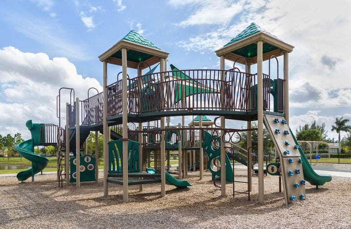 Engineered Wood Fiber Playground Surfacing beneath slides, climbing walls, and monkey bars with green roofs under a partly cloudy sky